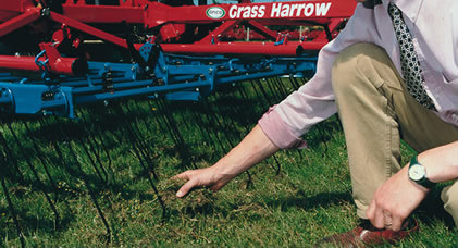 a photo of someone picking up grass cuttings next to a comb harrow